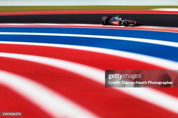 British McLaren Formula One team racing driver Lewis Hamilton driving his MP4-27 racing car at speed alongside red, white and blue ground painted...