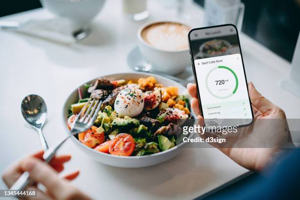close up of young woman using fitness plan mobile app on smartphone to tailor make her daily diet meal plan, checking the nutrition facts and calories intake of her beef cobb salad. maintaining a balanced diet. healthy eating lifestyle - gesunde nahrung stock-fotos und bilder