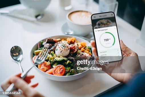 Close up of young woman using fitness plan mobile app on smartphone to tailor make her daily diet meal plan, checking the nutrition facts and calories intake of her beef cobb salad. Maintaining a balanced diet. Healthy eating lifestyle Close up of young woman using fitness plan mobile app on smartphone to tailor make her daily diet meal plan, checking the nutrition facts and calories intake of her beef cobb salad. Maintaining a balanced diet. Healthy eating lifestyle