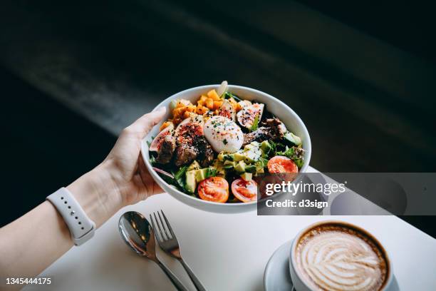 close up of woman's hand holding a bowl of fresh beef cobb salad, serving on the dining table. ready to enjoy her healthy and nutritious lunch with coffee. maintaining a healthy and well-balanced diet. healthy eating lifestyle - bowl foto e immagini stock