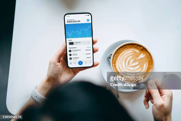 overhead view of young woman enjoying a coffee break, managing finance and investment, checking financial stock market data on smartphone in cafe. smart banking with technology - big tech foto e immagini stock