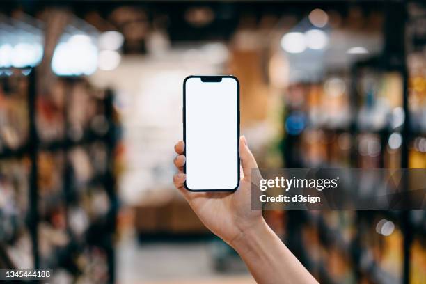 personal perspective of woman's hand holding a smartphone while grocery shopping in a supermarket, with product aisle in background. smartphone with blank screen for design mockup - uomo donna per mano foto e immagini stock