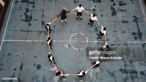 school children wearing uniform along with teachers standing holding hands in a circle shape - atrium grundstück stock-fotos und bilder