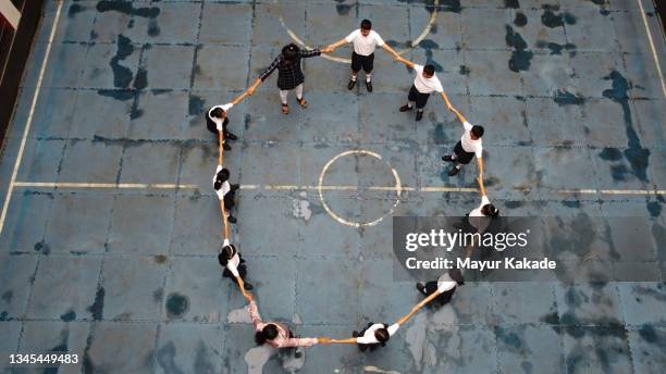 school children wearing uniform along with teachers standing holding hands in a circle shape - sports india stockfoto's en -beelden