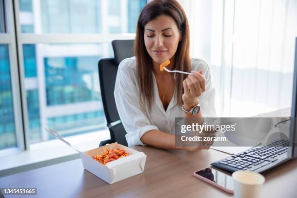 businesswoman eating delicious pasta on a lunch break - lunch break stockfoto's en -beelden