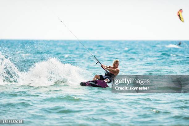 athletic man having fun while kitesurfing on the sea. - kite surfing stock pictures, royalty-free photos & images