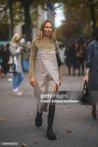 Alexandra Golovanoff wears a beige wool pullover, a beige suede gold and silver nailed / studded ruffled borders slit / split midi dress, a black...