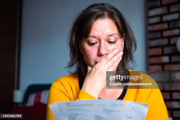 worried woman checking bills at home - bill stockfoto's en -beelden