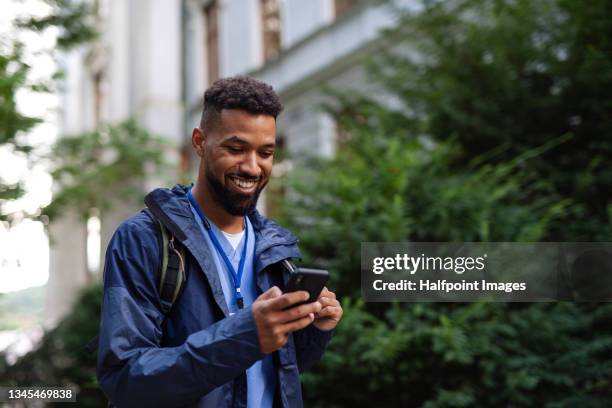 man caregiver, male nurse or healthcare worker outdoors on the way to work, using smartphone. - using phone foto e immagini stock