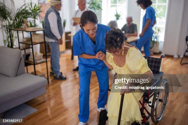 female nurse helping senior woman to get up from wheelchair in nursing home - assisted living community stock pictures, royalty-free photos & images