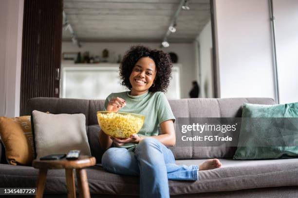 young holding a bowl of popcorn and watching tv at home - brazil girls supporters stock pictures, royalty-free photos & images