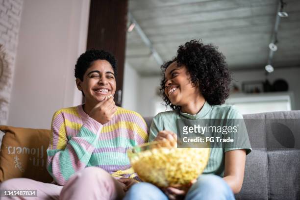 friends watching tv and eating popcorn at home - family watching tv together stock pictures, royalty-free photos & images