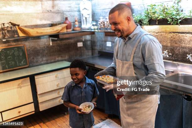 father and son serving food together at home - fathers day lunch stock pictures, royalty-free photos & images