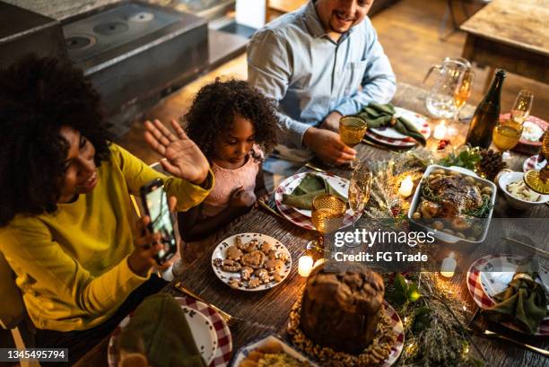 young woman doing a video call with her family on christmas dinner at home - christmas zoom stock pictures, royalty-free photos & images