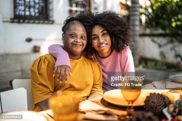 Portrait of sisters embracing at lunch time at home outdoors - including special needs woman