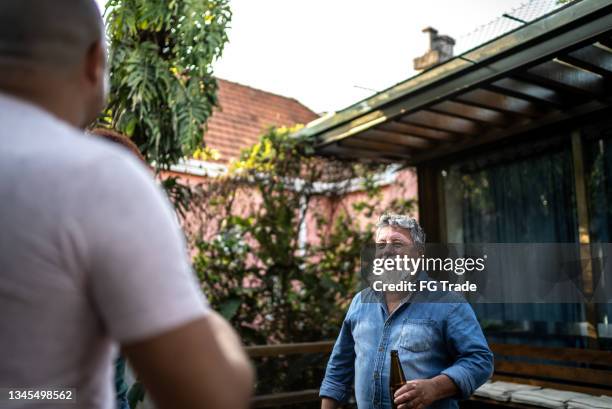 älterer mann spricht und hält eine bierflasche zu hause - nachbarn stock-fotos und bilder