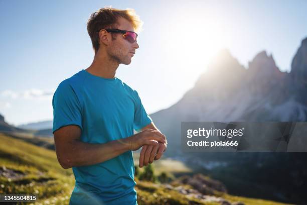 young man trail running on the mountain, looking sport watch - shade stock pictures, royalty-free photos & images