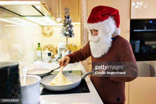 little santa claus making christmas crepes pancakes in kitchen - santa pancakes stock pictures, royalty-free photos & images
