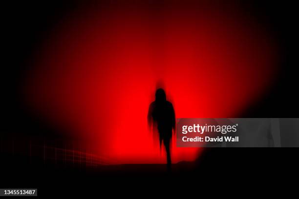 a dark, horror concept. of a blurred hooded figure silhouetted against lights at night. with a black, red moody edit. - spooky stock-fotos und bilder
