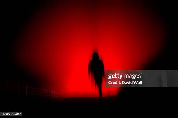 a dark, horror concept. of a blurred hooded figure silhouetted against lights at night. with a black, red moody edit. - fantasma foto e immagini stock