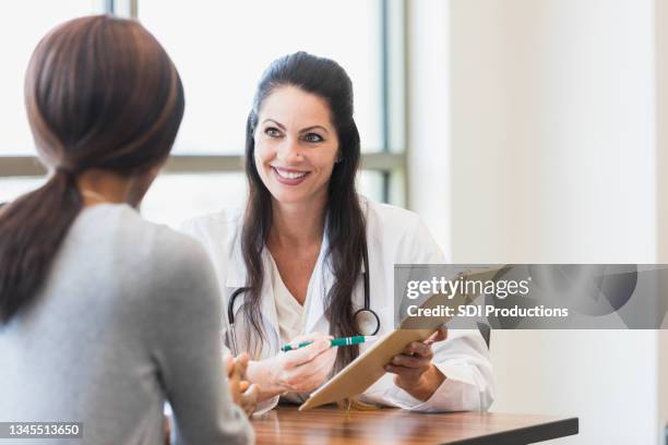 female doctor smiles while listening to unrecognizable female patient - gynecology stock pictures, royalty-free photos & images