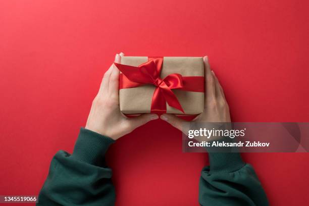 a girl in a green sweater holds a beautiful surprise gift box tied with a bright ribbon on a red background. a woman opens gifts on her holiday. the concept of merry christmas, birthday, valentine's day. copy space. - gift lounge foto e immagini stock