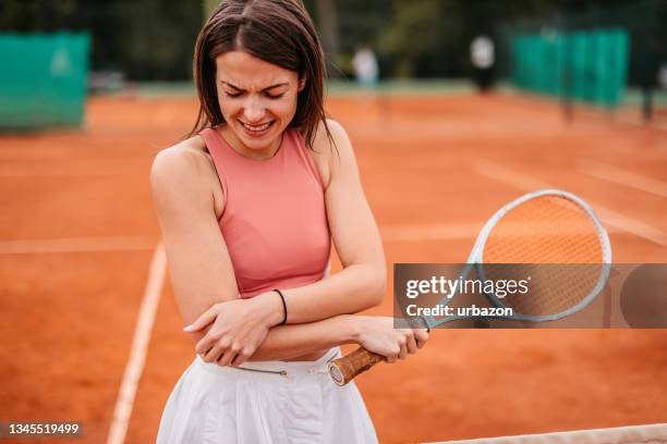 woman holding elbow in pain while playing tennis - elleboog stockfoto's en -beelden