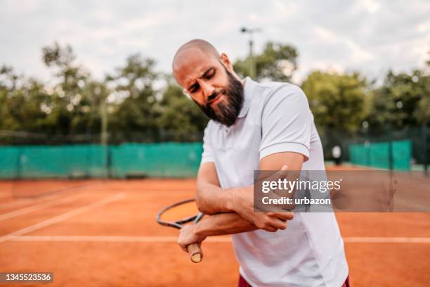 man holding elbow in pain while playing tennis - amateur tennis man stock pictures, royalty-free photos & images