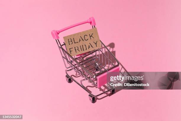 metal and pink shopping cart, with brown black friday sign with hard shadow, on pink background. shopping, discounts, opportunities and black friday concept. - black friday foto e immagini stock