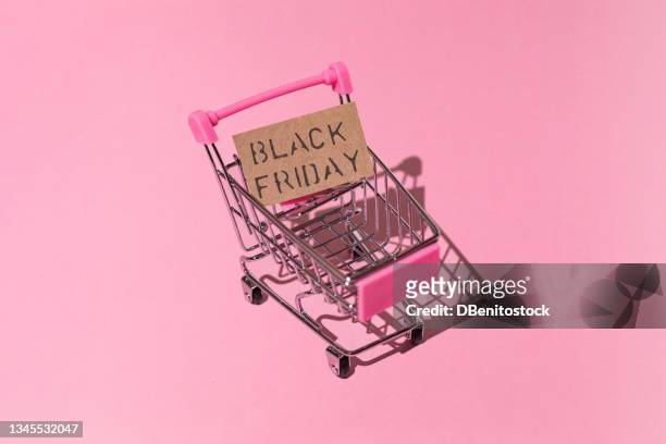 metal and pink shopping cart, with brown black friday sign with hard shadow, on pink background. shopping, discounts, opportunities and black friday concept. - black friday sale stock pictures, royalty-free photos & images