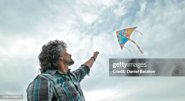 mature man flying kite in moody sky. childhood fun. low angle vi - kite flying stock pictures, royalty-free photos & images