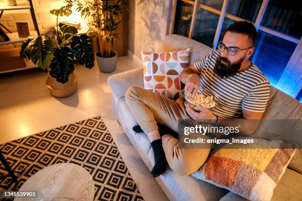 man watching television eats pop corn - stress eating stock pictures, royalty-free photos & images