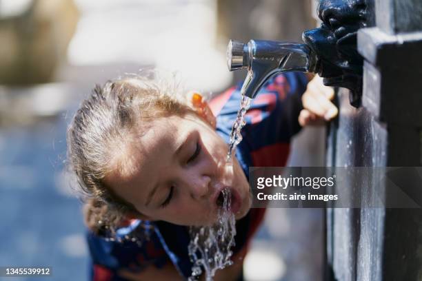 a little girl leans to drink some water directly from a water dispenser. a little girl drinks water from a public water line in spain. - hands fountain water stock-fotos und bilder