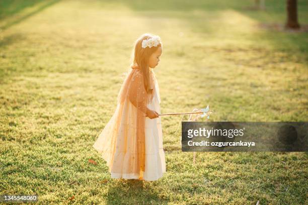 little girl dressed in a fairy's outfit prances over the green grass holding a wand - angel white dress stock pictures, royalty-free photos & images