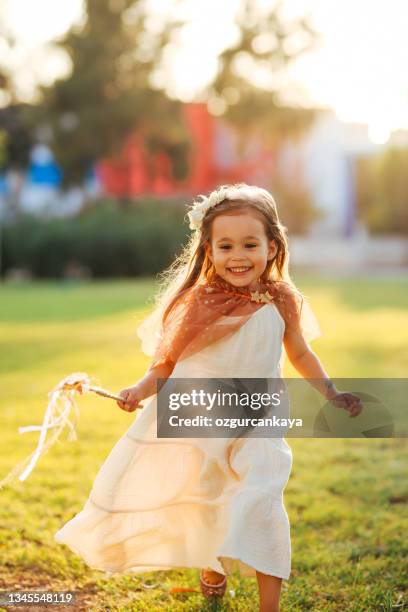 little girl dressed in a fairy's outfit prances over the green grass holding a wand - angel white dress stock pictures, royalty-free photos & images