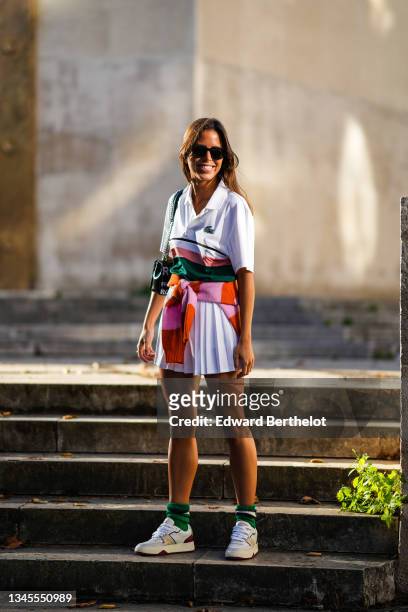 Guest wears sunglasses, a white with large pink and dark green polo shirt from Lacoste, a pink and orange striped fluffy wool pullover knotted on the...