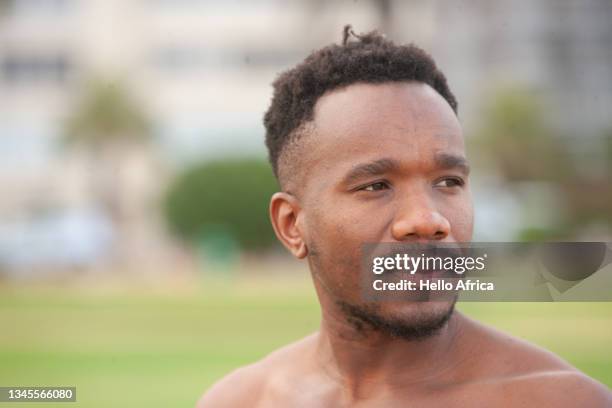a handsome pensive, perhaps serious business young man looks out from a green lawn with palm trees and other lush vegetation in the background of an urban park - goatee stockfoto's en -beelden