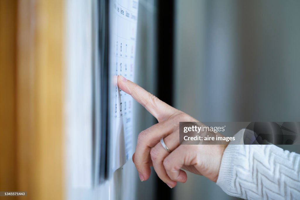A woman's hand with a wedding ring points with her finger to a date on a cardboard calendar. A woman points to a calendar's day