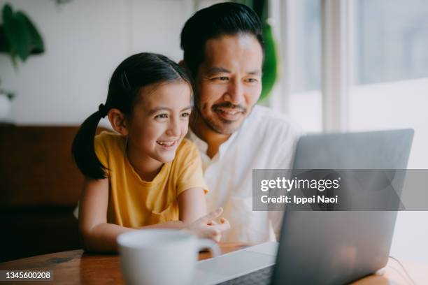 father and young daughter on video call on laptop at home - familie laptop stock-fotos und bilder