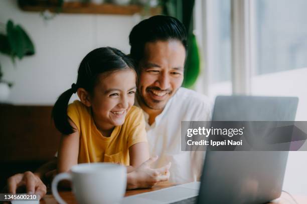 father and young daughter on laptop video call at home - familia de dos generaciones fotografías e imágenes de stock