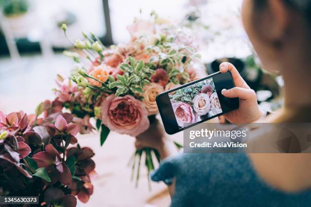 joven florista asiática, dueña de una floristería de una pequeña empresa, tomando fotos de un hermoso ramo. actualización y publicación en su tienda en línea y venta de productos en línea. dirigir un negocio en línea, comercio electrónico, compra - asia lady selling flower fotografías e imágenes de stock