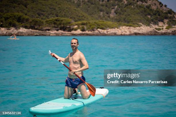 man paddle surfing in the middle of a turquoise sea - paddle board men imagens e fotografias de stock