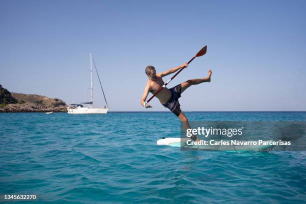 man falling from the paddle surf board in the middle of the sea - fall stock-fotos und bilder