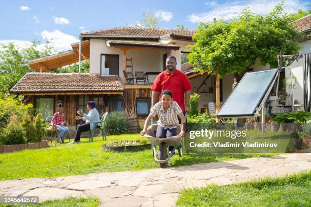 afro-american dad is driving his son in a whellbarrow - jamaican culture stock pictures, royalty-free photos & images