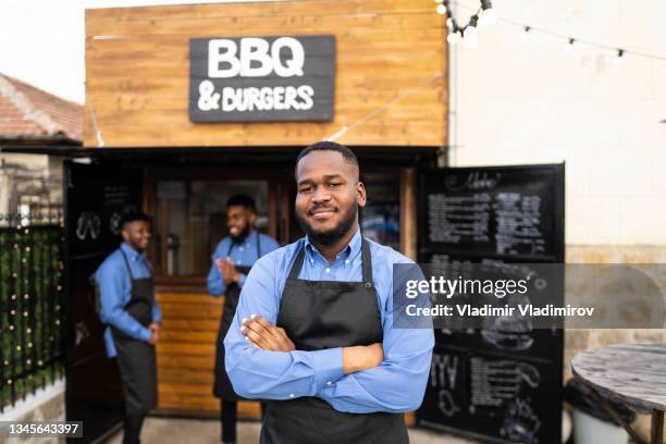 a happy waiter, outside a restaurant standing with his arms folded - restaurants open during lockdown stock pictures, royalty-free photos & images