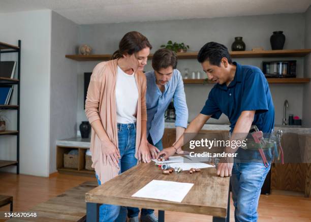 plumber fixing a pipe and talking to his clients in the kitchen - renovatie begrippen stockfoto's en -beelden