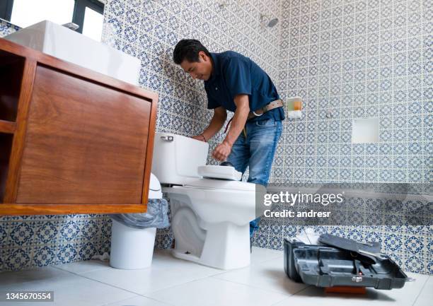 latin american plumber fixing a toilet in the bathroom - loodgieter stockfoto's en -beelden