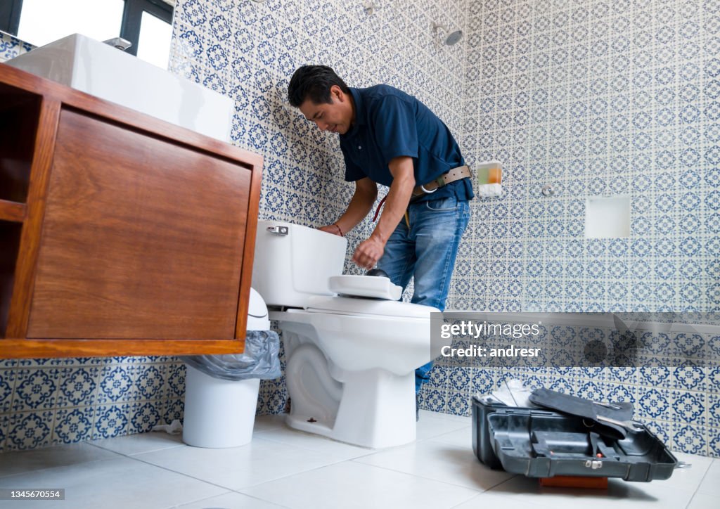 Latin American plumber fixing a toilet in the bathroom