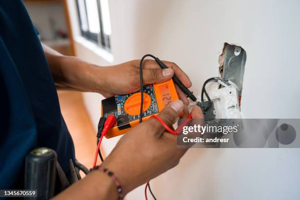 electricista arreglando una toma de corriente y midiendo el voltaje - arreglar fotografías e imágenes de stock