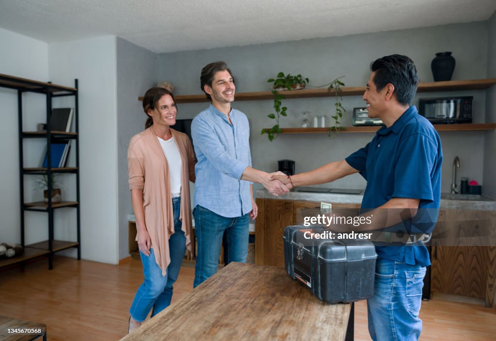 Plumber greeting happy clients at home with a handshake